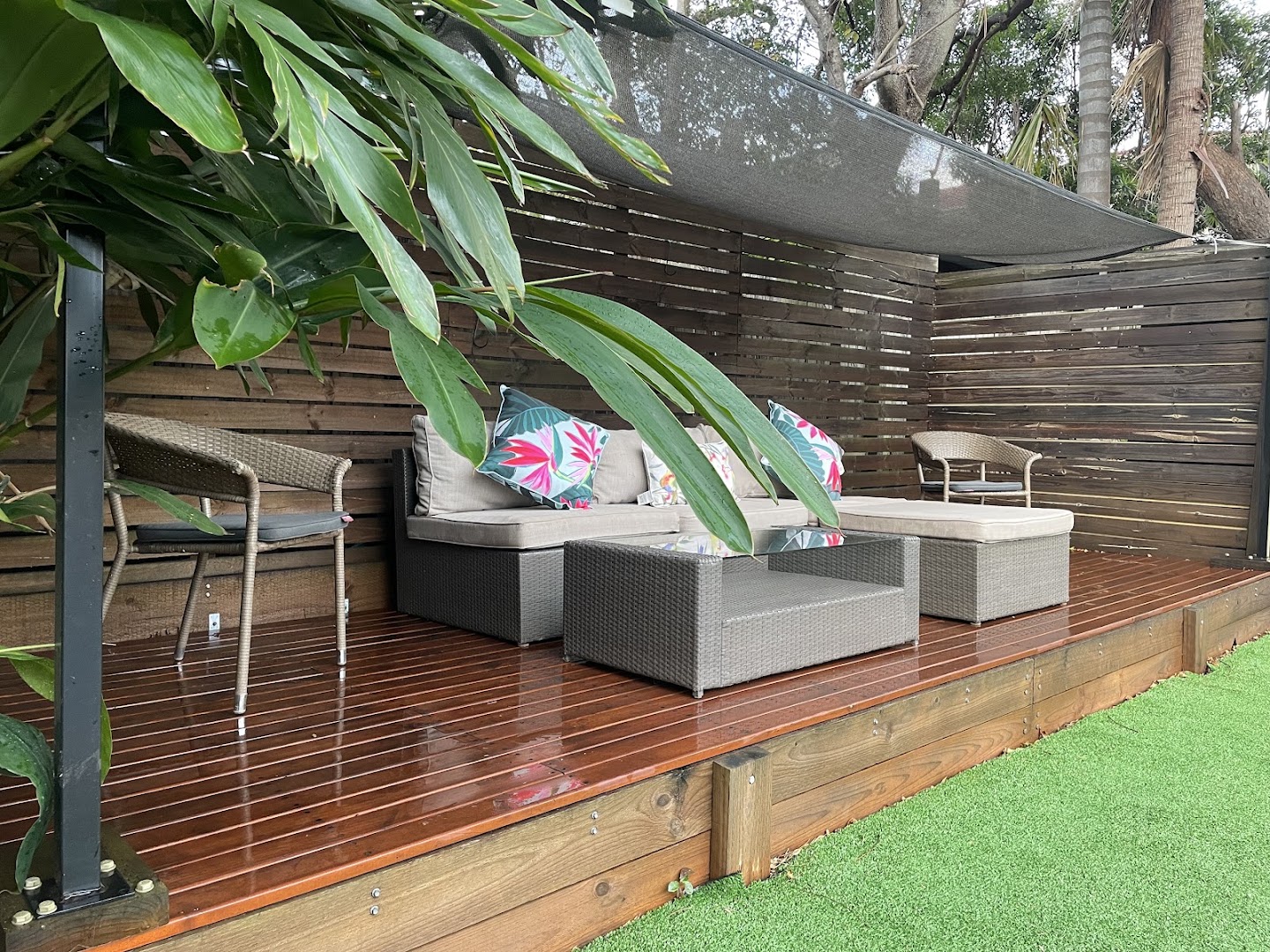 An oiled timber deck with an outdoor lounge setting under a slatted privacy screen