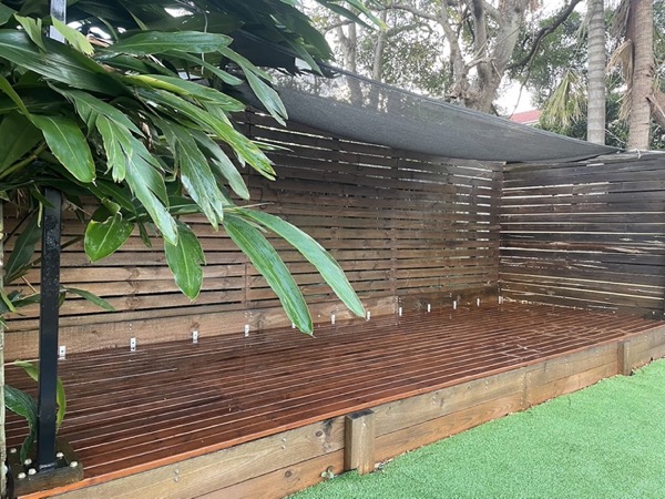 A long oiled timber deck with a horizontal slatted privacy screen along one side