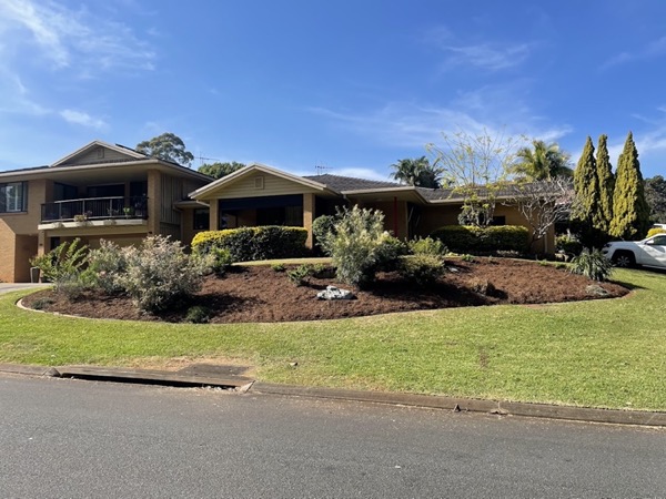 A brick home behind a cut front lawn and a fresh mulched garden bed