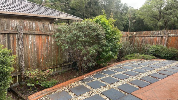 Square pavers set in gravel forming a path along a timber fence line
