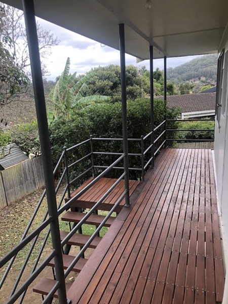 An oiled timber deck and stair landing with a steel handrail beside a house