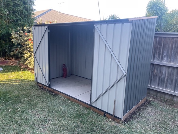 A steel garden shed standing on a level base with both doors open