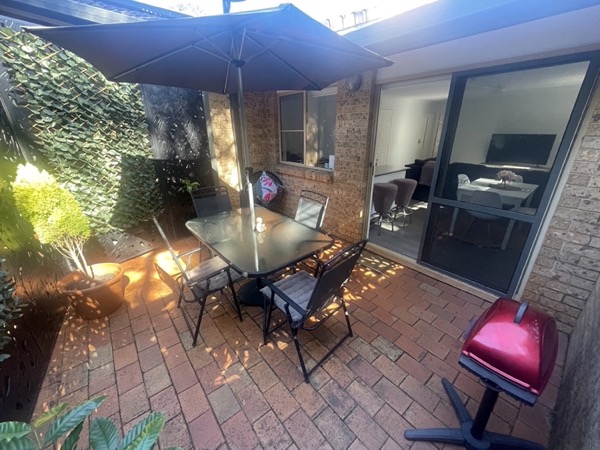 A paved courtyard with an outdoor table and chairs beside a home office window
